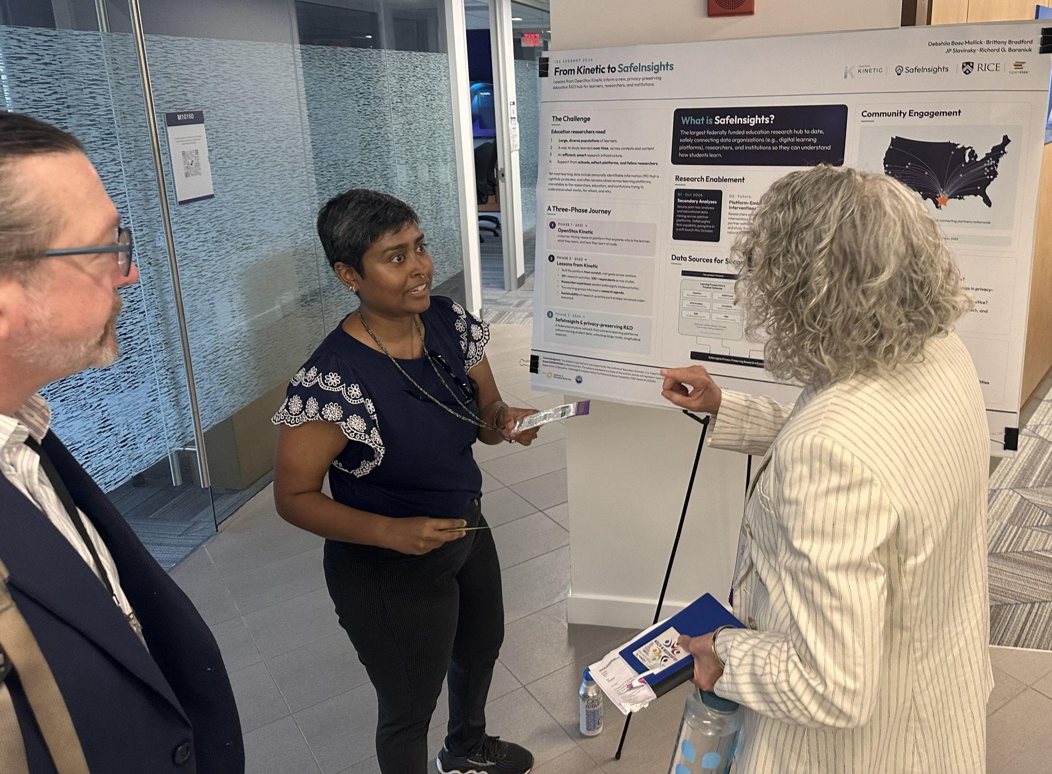 Two women and a man standing next to a research poster while engaging in a conversation